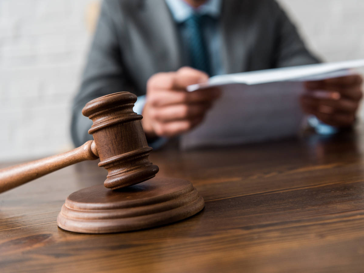 Judge gavel in foreground with person in suit presenting a forensic psychology report in background