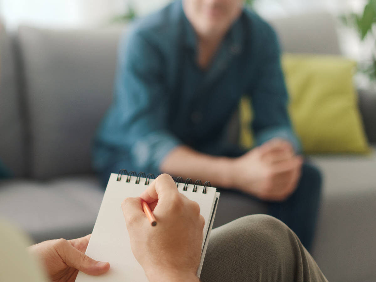 person sitting in couch getting a psych evaluation in westport ct, with a hand writing in a notebook in the foreground